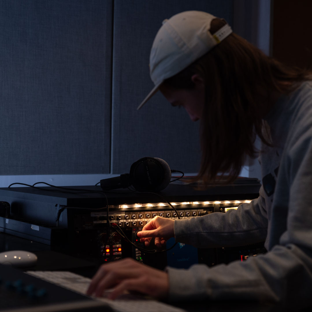 Musikkproduksjon-student jobbar konsentrert med å finne rette nivå på lydmiksaren