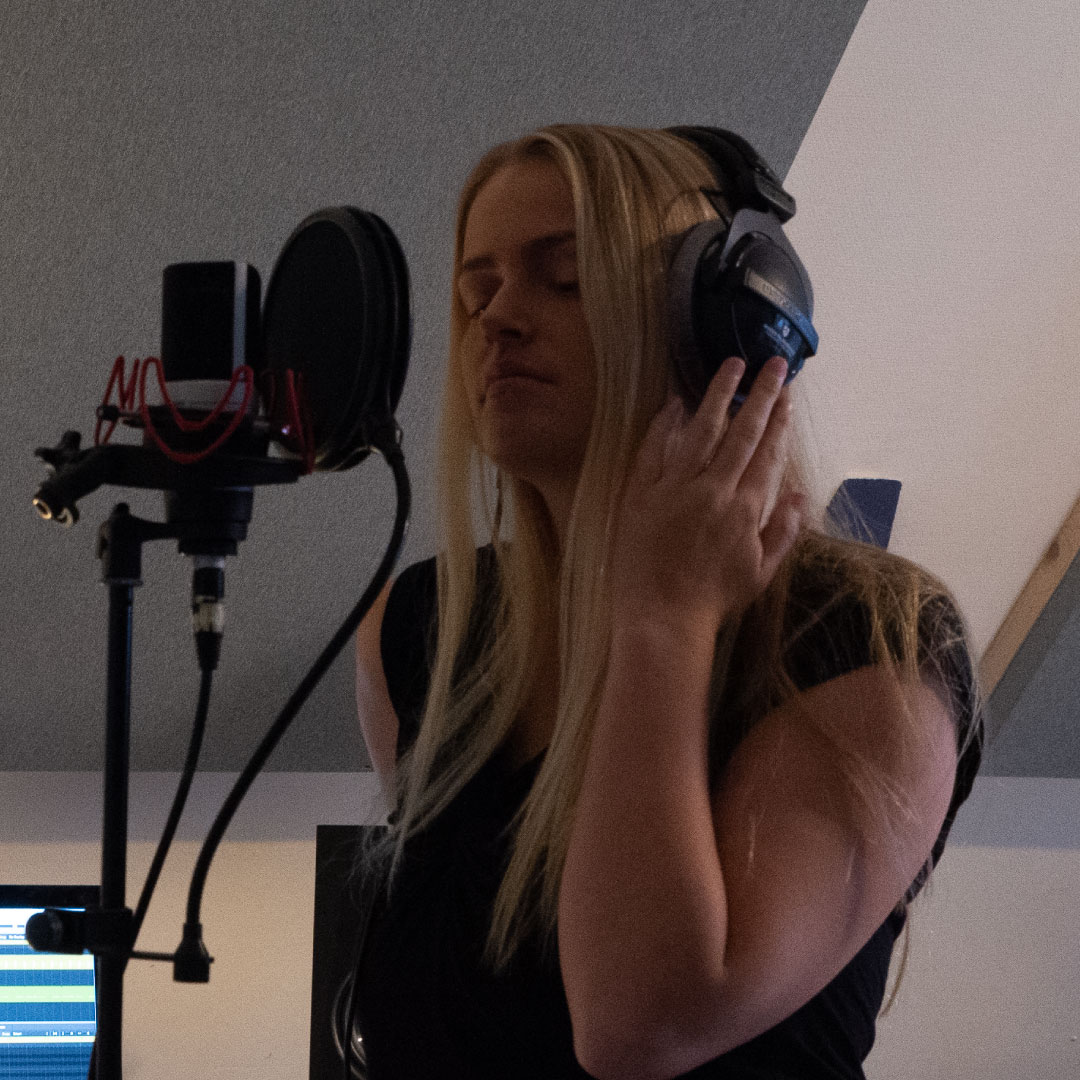 Jente syng ein song i studio med høyretelefonar på hovudet